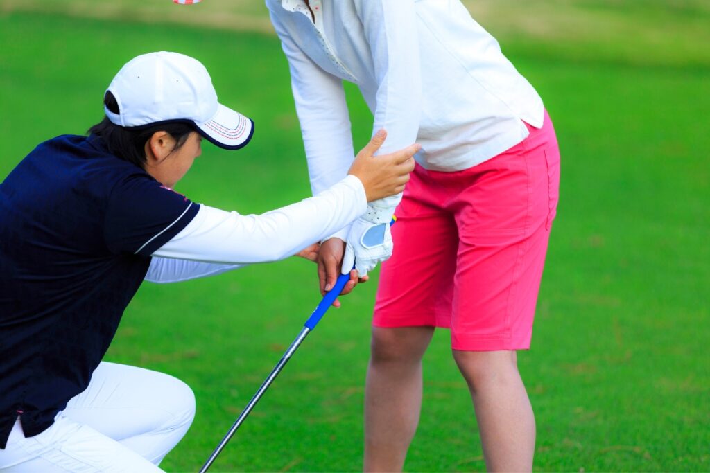 A woman is assisting a young girl in golf.
