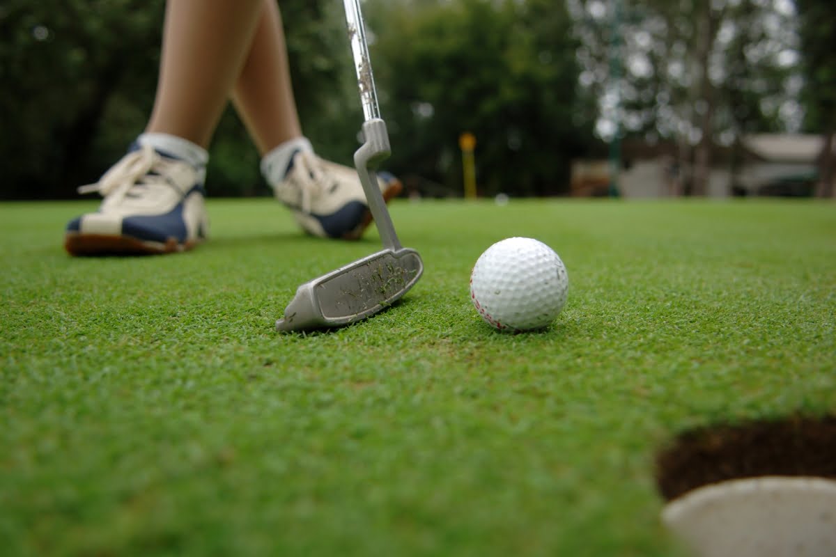 A compression golf sock-clad golfer expertly putts a golf ball on a pristine green golf course.