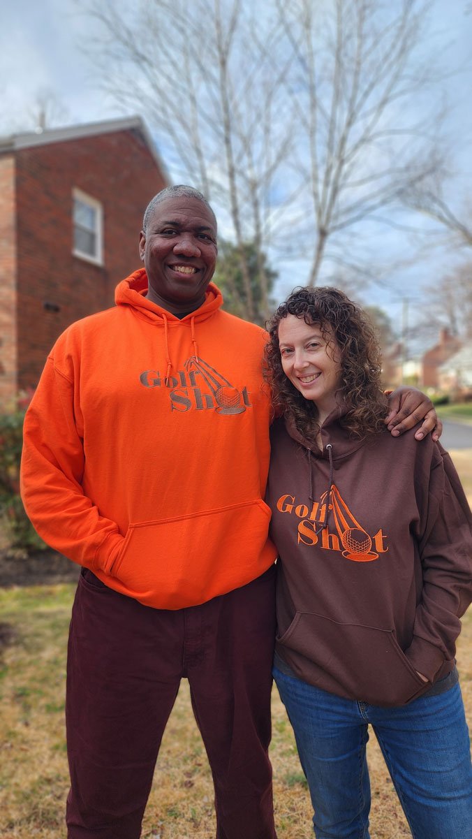 A man and woman standing in front of a house wearing orange hoodies.