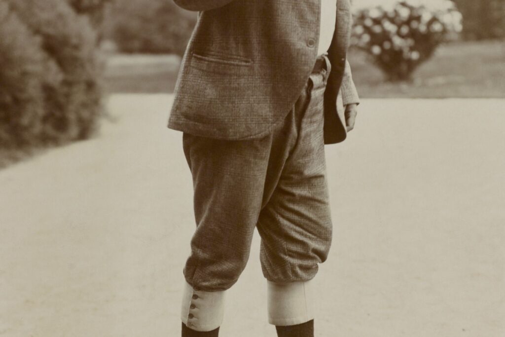 A young man in a suit and tie exhibiting the history of golf attire by holding a cigarette.