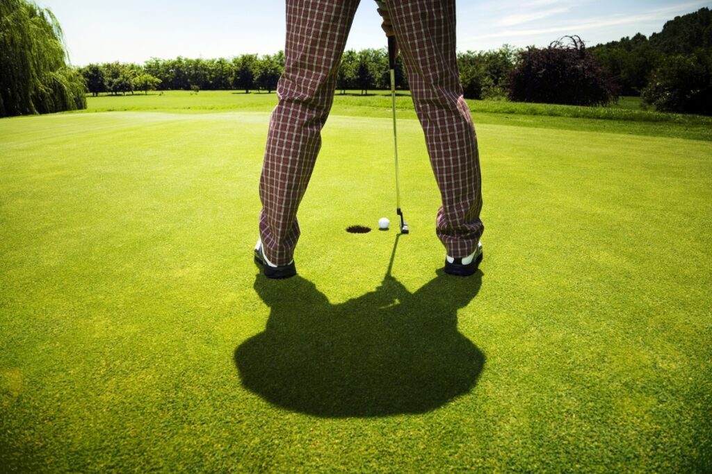 A man is standing on a golf course wearing golf lifestyle apparel and holding a golf club.