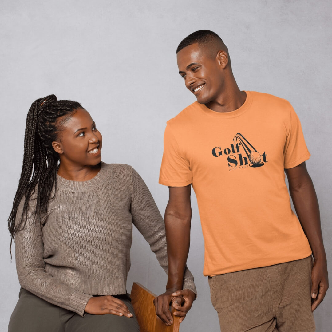 A woman sits on a wooden chair smiling at a man standing next to her, who is wearing an orange "Golf Shot" t-shirt and smiling back at her.