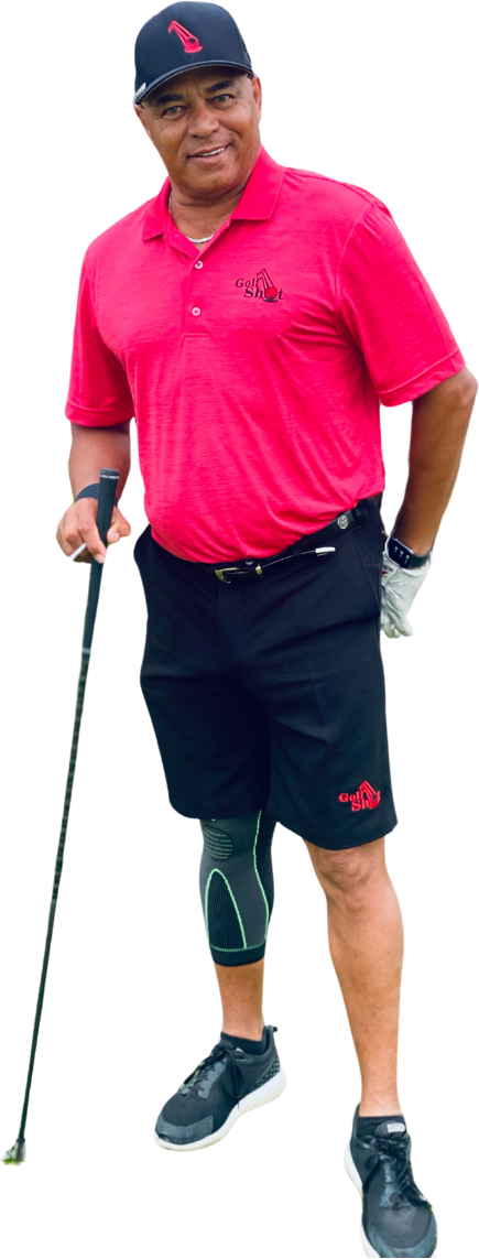 Man in a red shirt and black shorts holds a golf club and wears a knee brace, white glove, black cap, and black sneakers.