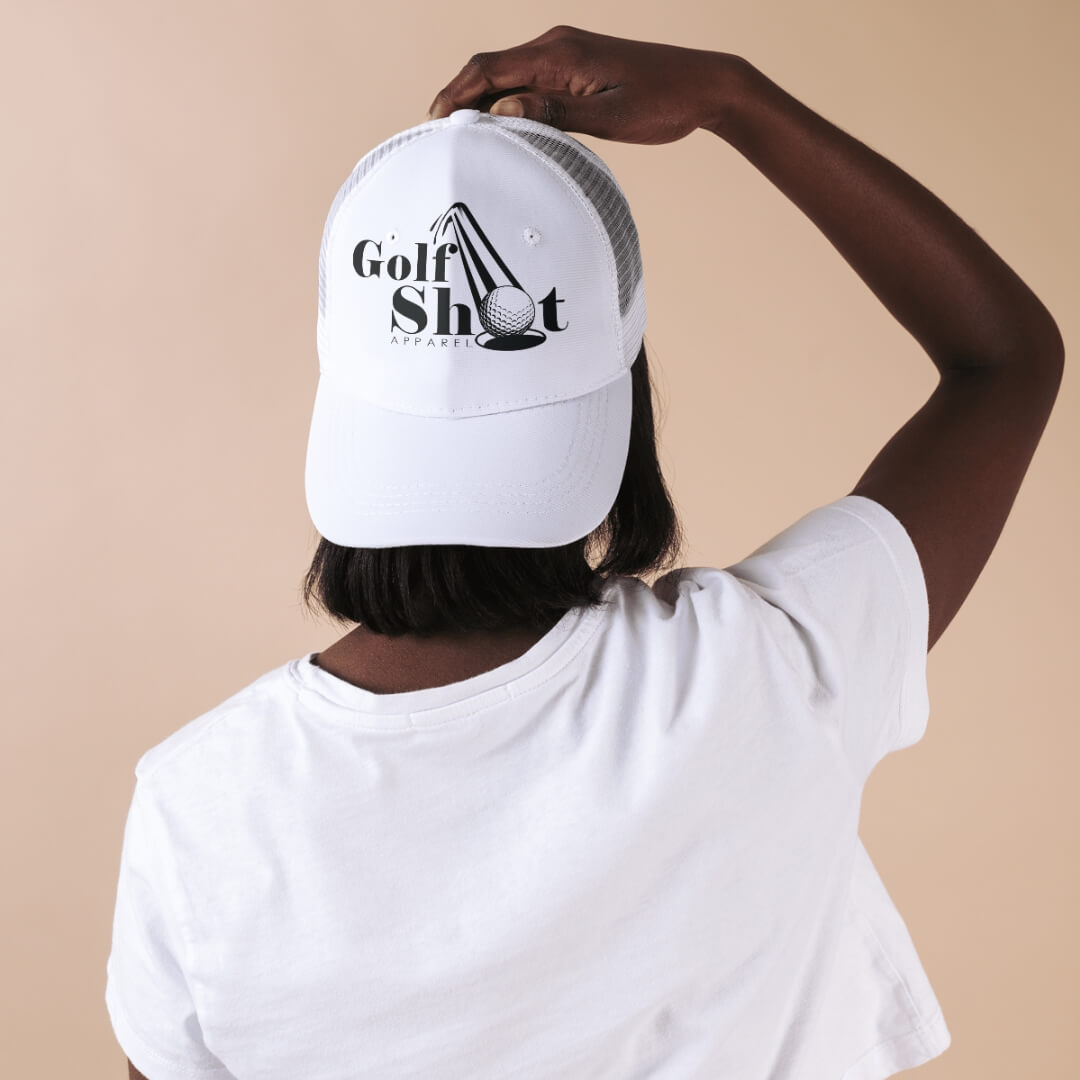 Person wearing a white "Golf Shot Apparel" cap and a white t-shirt, photographed from behind with a hand touching the cap.